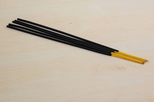 Black agarbatti, also known as incense sticks, rest on a wooden background. Incense is a substance that releases fragrant smoke when burned. It finds use in religious rituals, meditation, and more.